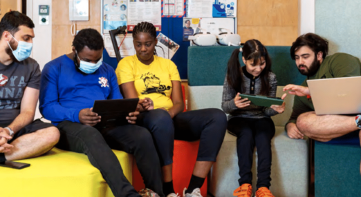 Five people on comfortable chairs looking at devices